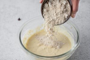 Adding dry ingredients for banana cookies with chocolate chips, from smaller bowl to bigger
