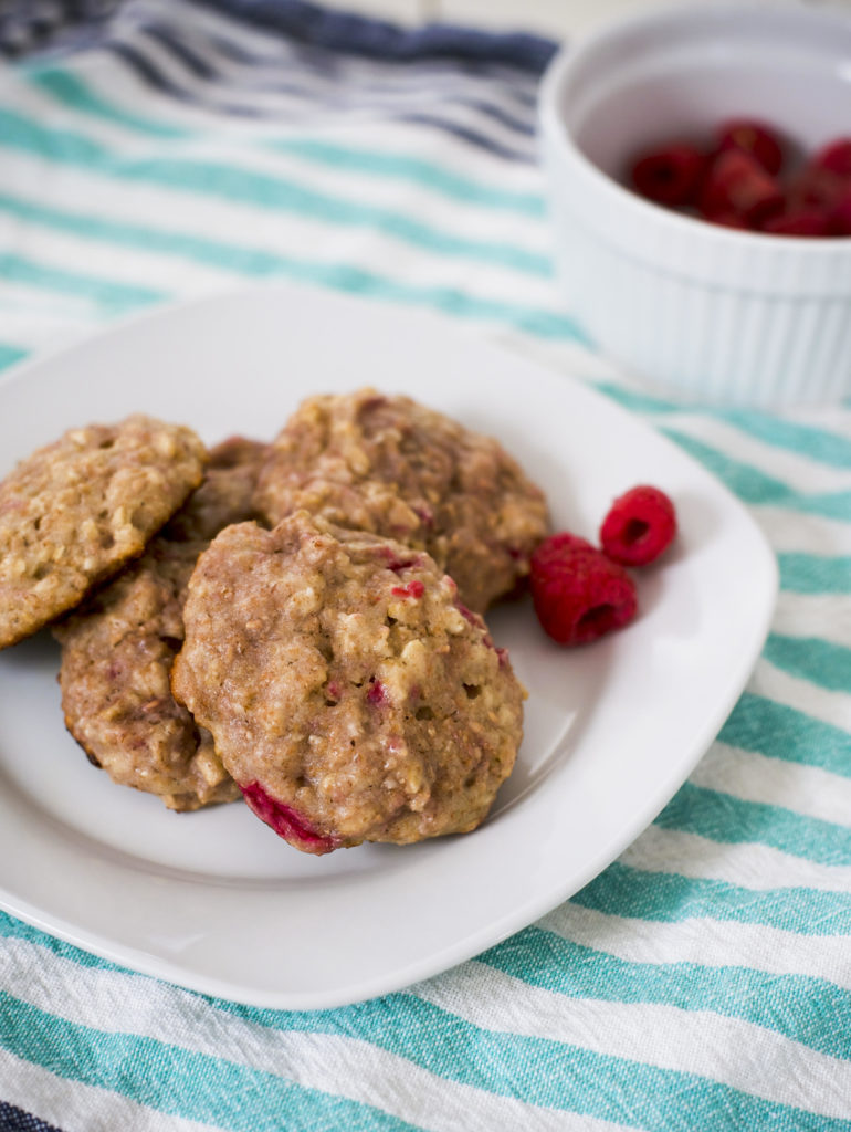 breakfast cookies on a white plate next to a bowl of raspberries