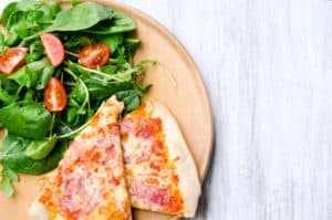 Pizza slices on plate with fresh side salad, overhead perspective with plenty of copy space on rustic white background