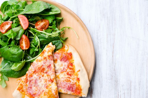 Pizza slices on plate with fresh side salad, overhead perspective with plenty of copy space on rustic white background