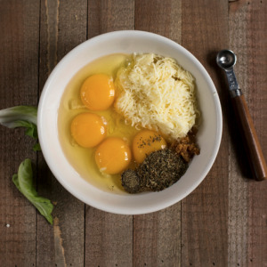 eggs, cheese, seasoning, and garlic in a white bowl with a measuring spoon