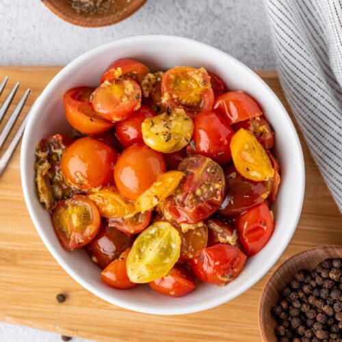 Parmesan tomato bites in a bowl that is on the cutting board with a bowl of pepper beside and a fork