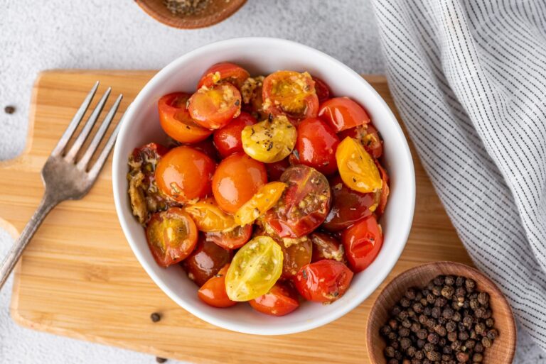 Parmesan tomato bites in a bowl that is on the cutting board with a bowl of pepper beside and a fork