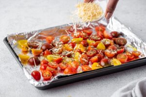 Tomatoes cut in half on a foil that are being drizzled with grated parmesan cheese
