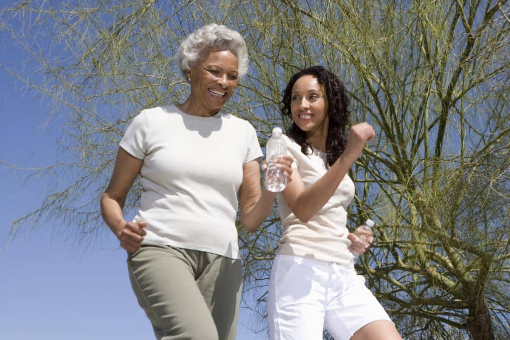 Happy African American mother and daughter jogging together against blue sky
