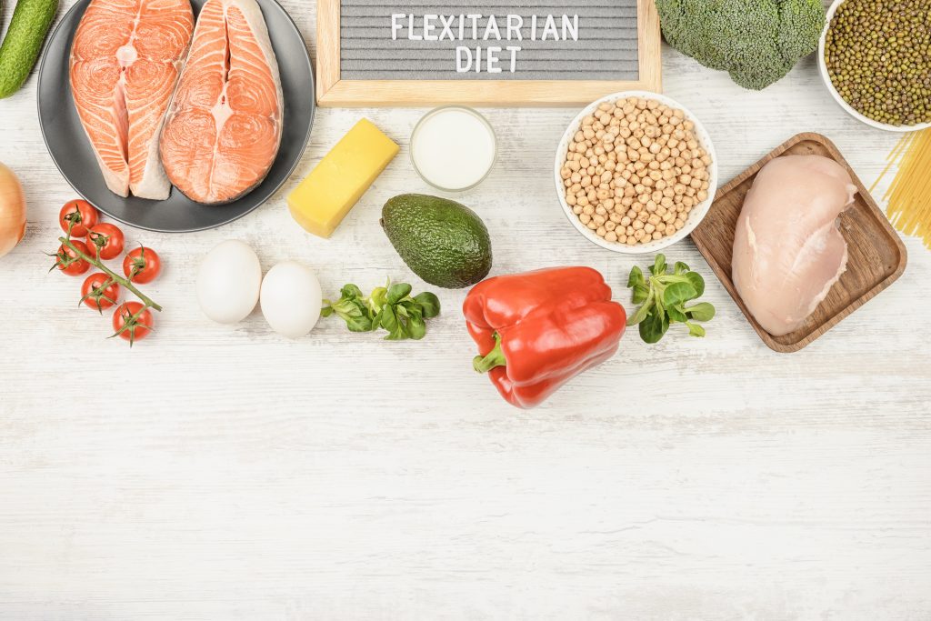 On a light background, cereals, vegetables, eggs, salmon and chicken are beautifully laid out. A plate with the words Flexitarian diets, around half-eaten foods. Copy space for text.