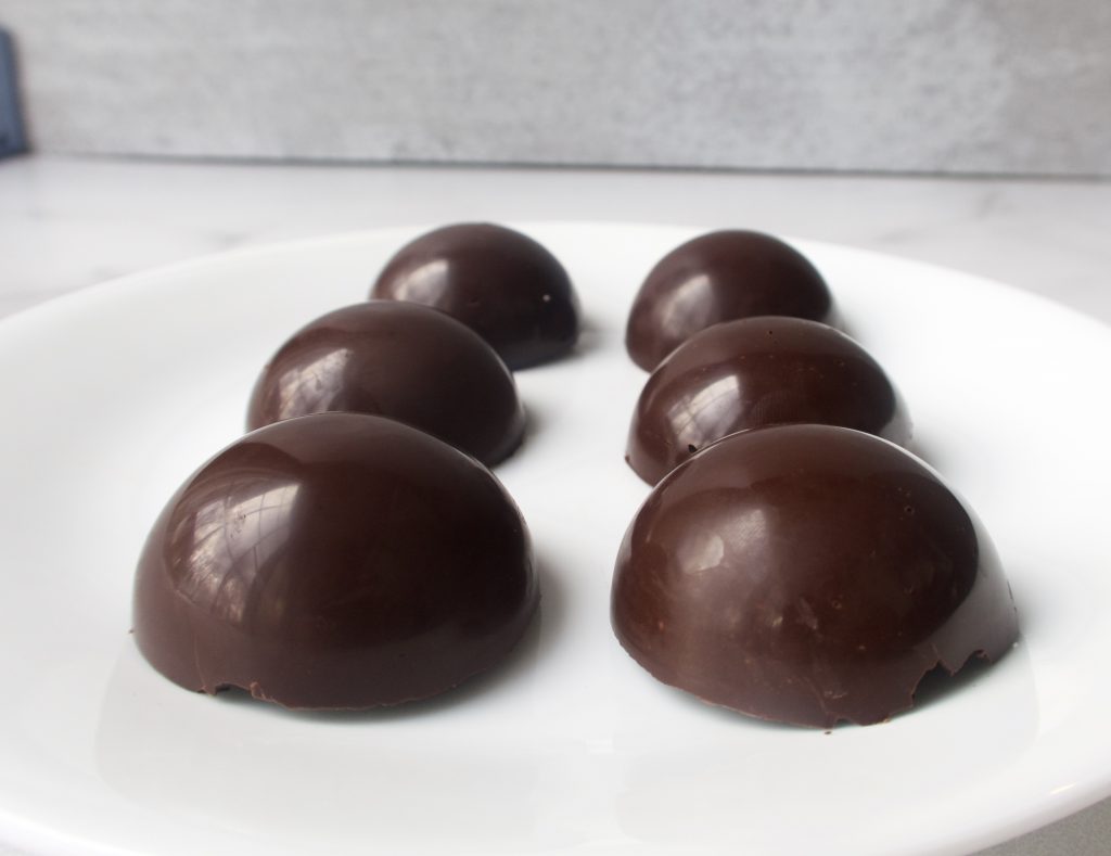 6 plain round chocolate shells on a white plate