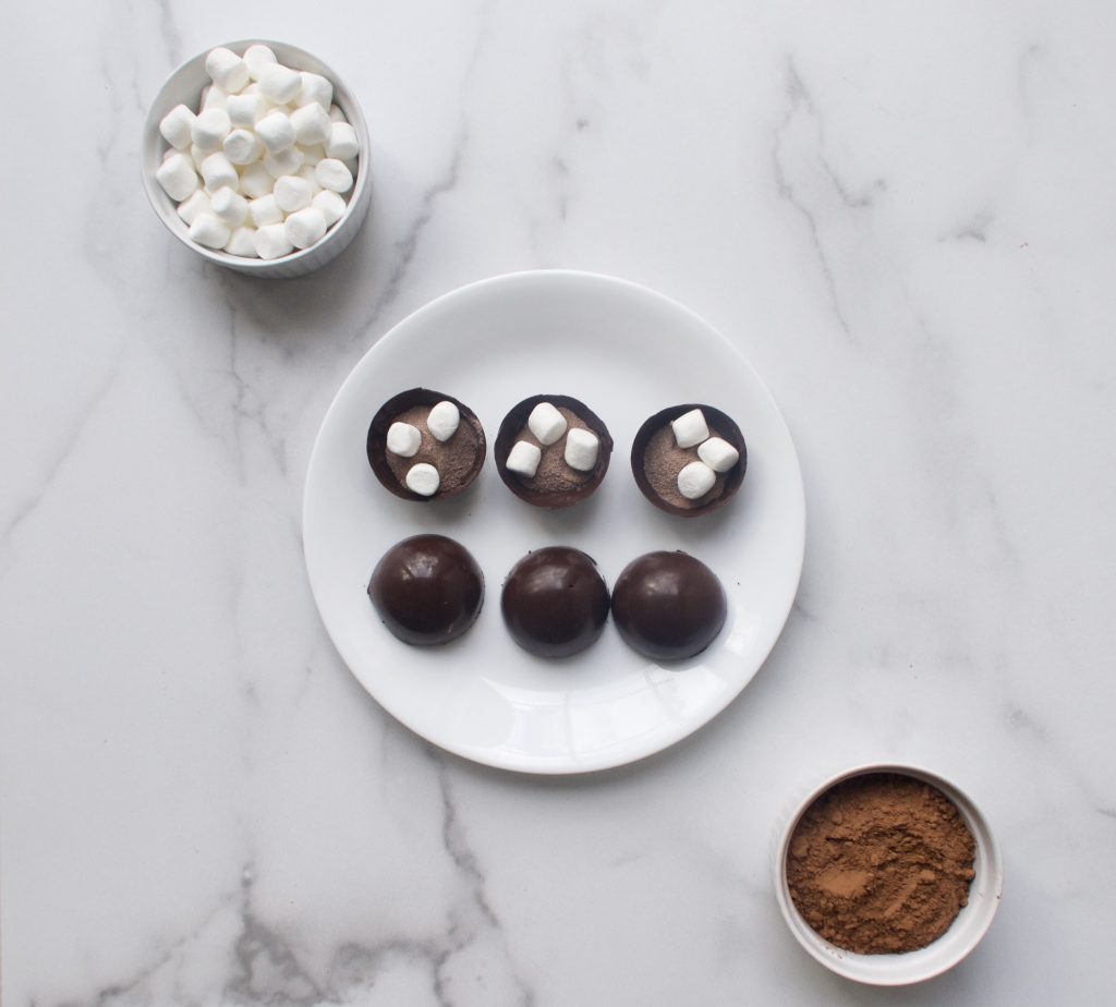 ingredients on a hot chocolate bomb on white plates and bowls on a marble surface