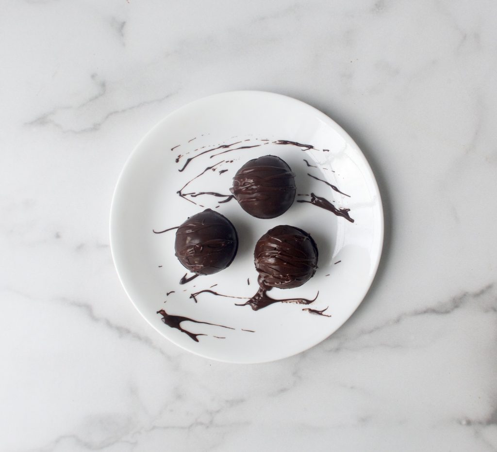 3 hot chocolate bombs on a white plate with a chocolate drizzle on a marble surface