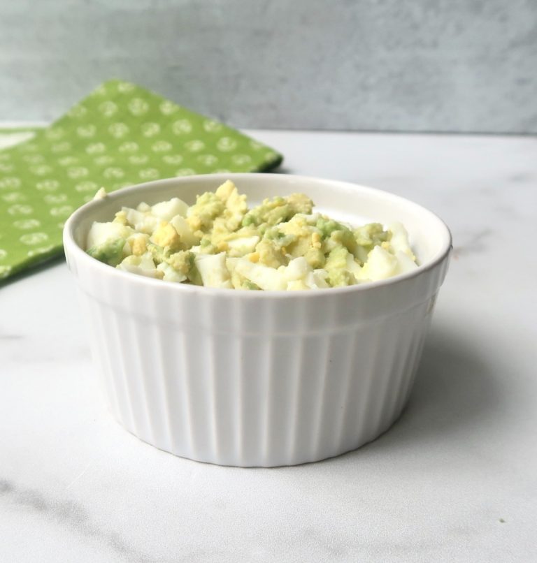Avocado egg salad in white ramekin on marble counter with green towel in background