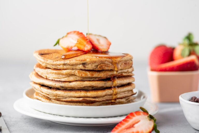 Greek yogurt pancakes on top of each other served on the plate with sliced strawberry on top and dressed with syrup
