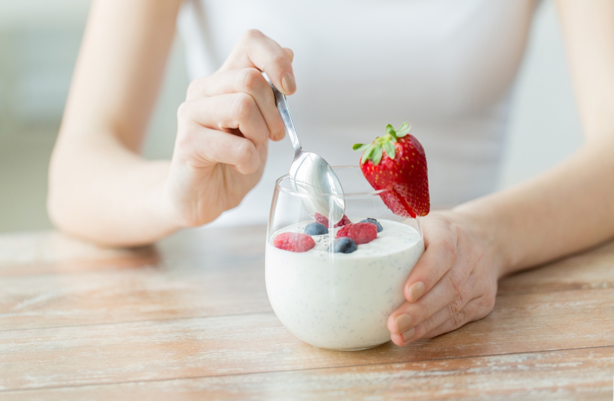 Woman holding a spoon, preparing to eat yogurt with fruits in the glass, on the table