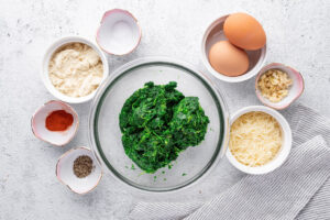 ingredients for spinach pancakes in small bowls on a white backdrop