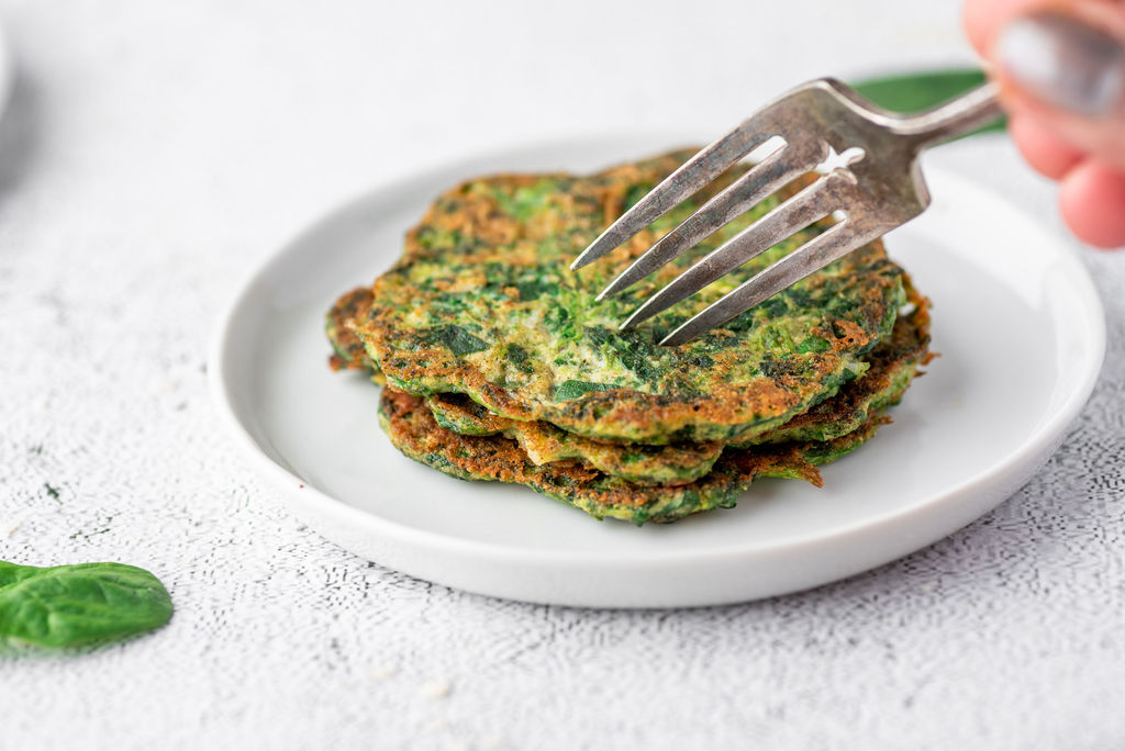 fork cutting into a stack of spinach pancakes on a white plate