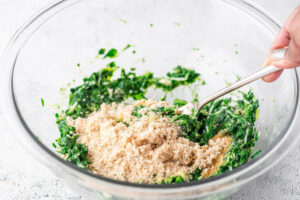 spinach, flour, eggs, and spices mixed together with a fork in a glass bowl