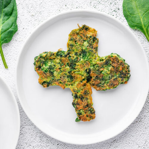 spinach pancake in the shape of a clover on a white plate with fork