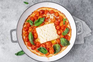 Backed feta cheese with cherry tomatoes, olive oil and basil in cooking pan