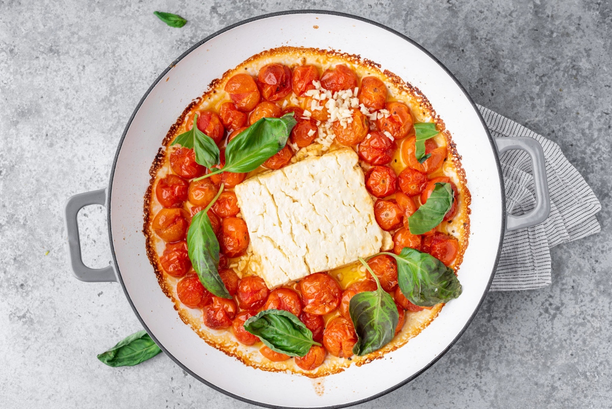 Backed feta cheese with cherry tomatoes, olive oil and basil in cooking pan
