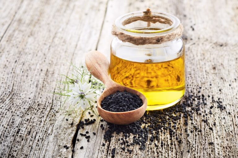 Black seed oil in the jar and a spoon with black seeds beside, with sprinkled black seeds around them