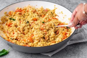Hand using fork o toss and combine rice with feta, cherry tomato and basil in cooking pan