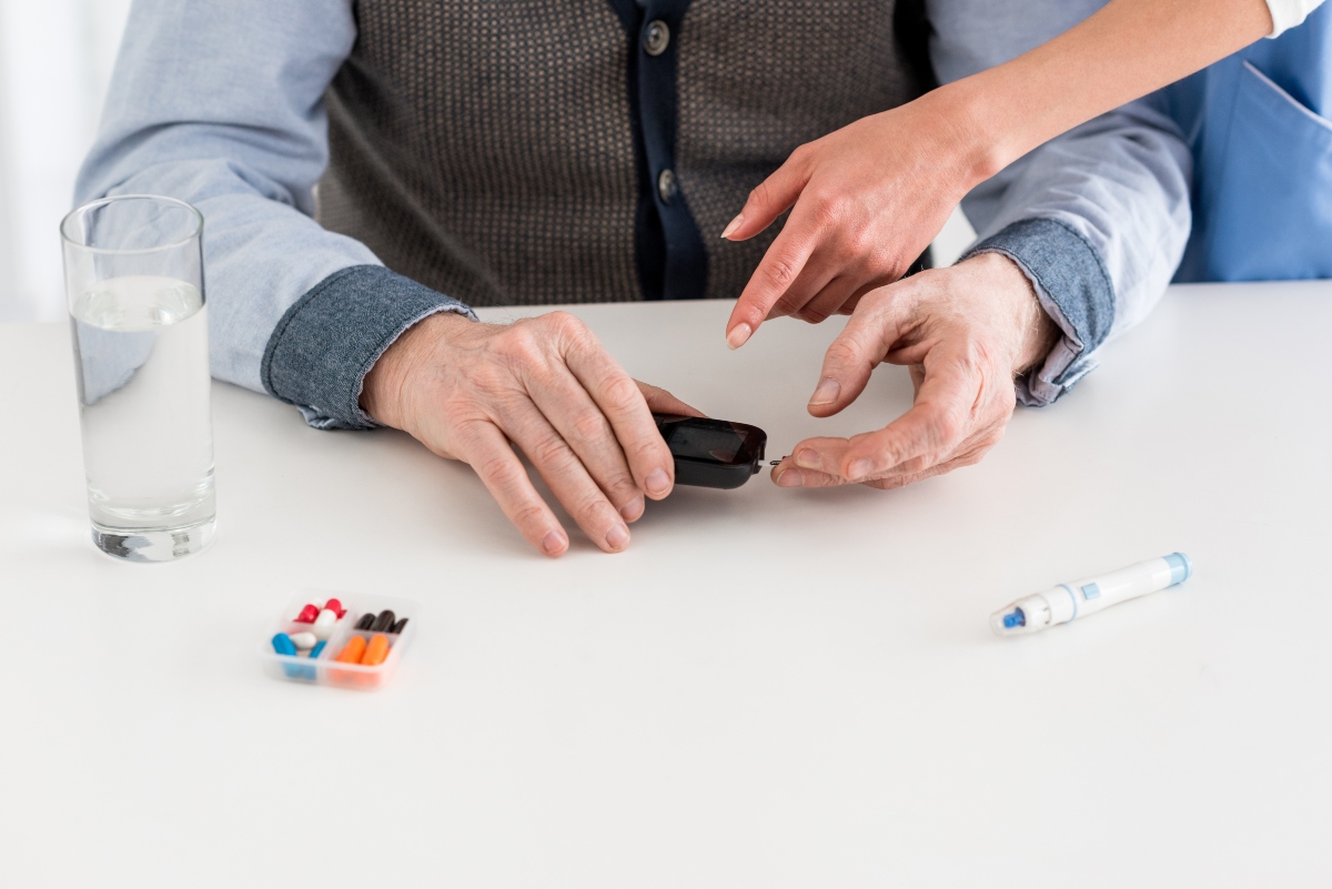 Man's hand holding blood sugar meter and woman's hands showing how to use it with pills beside