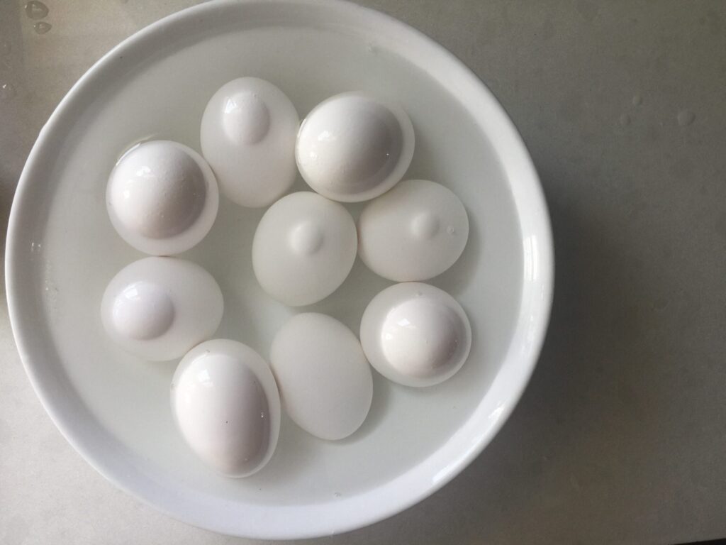9 hard boiled eggs submerged in water in a white bowl