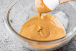 melted peanut butter in a glass bowl being stirred with a spatula