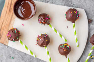 chocolate covered cake pops with green and white straws on a parchment paper topped with sprinkles