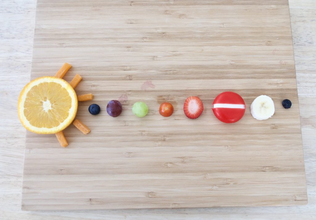 various fruits and veggies representing the solar system on a cutting board