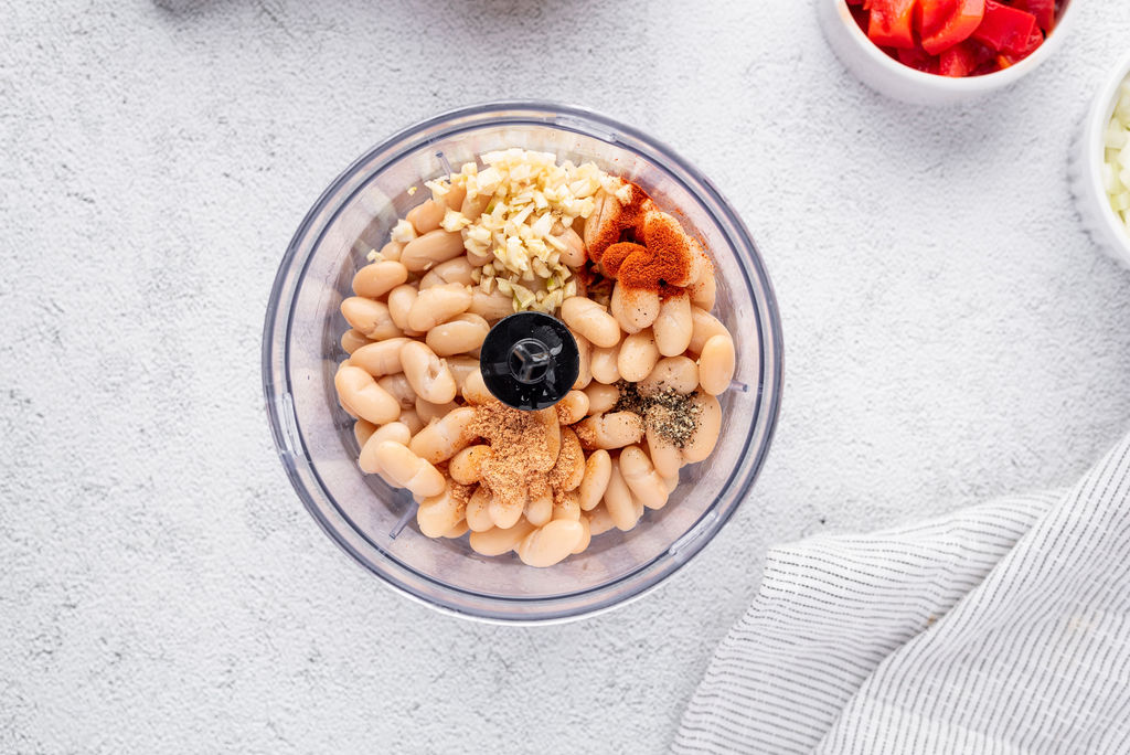 white beans with garlic and spices in a food processor on a white back drop