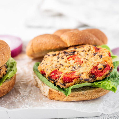 2 veggie burgers on buns with lettuce with red onion in background