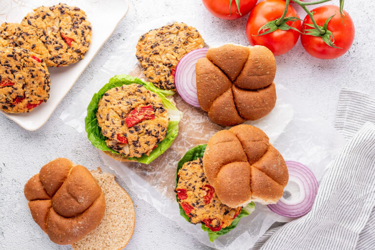 6 bean burger patties on buns and on plates with toppings and tomatoes on the vine