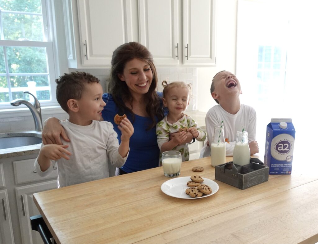 mom with three young children eating milk and cookies while laughing in kitchen