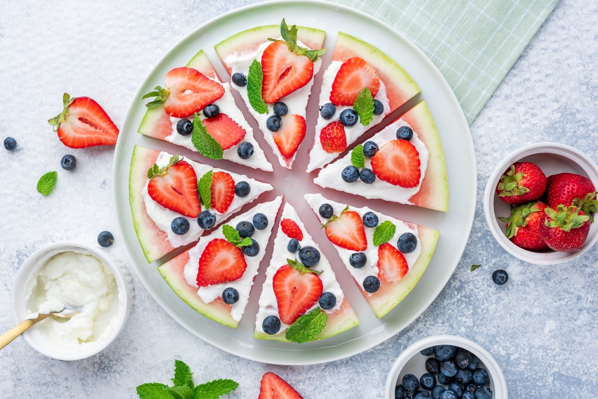 Watermelon pizza served on a plate with strawberries, Greek yogurt and blueberries in the cups around the plate