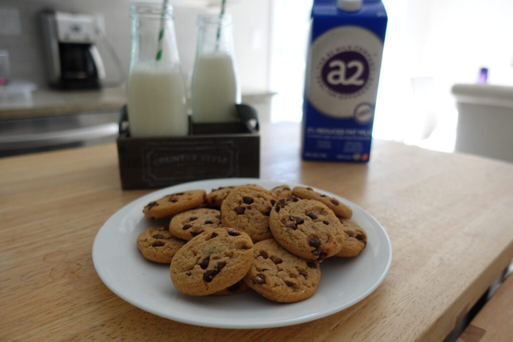 white plate filled with chocolate chip cookies with glass jars of milk and carton in background