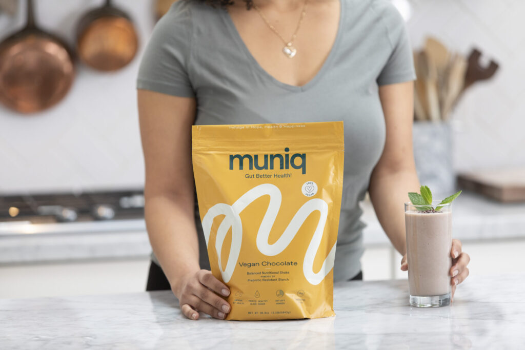 woman's hand on bag of Muniq shakes next to chocolate smoothie in glass