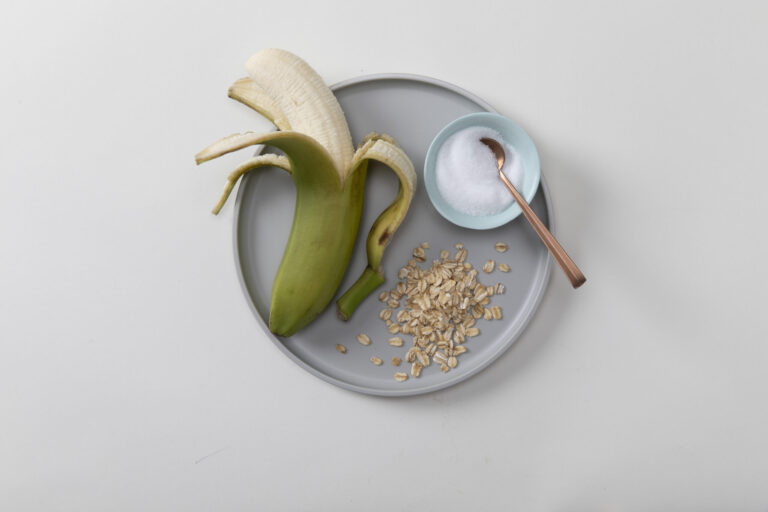 partially peeled banana, yogurt with spoon, and oat flakes on circular plate