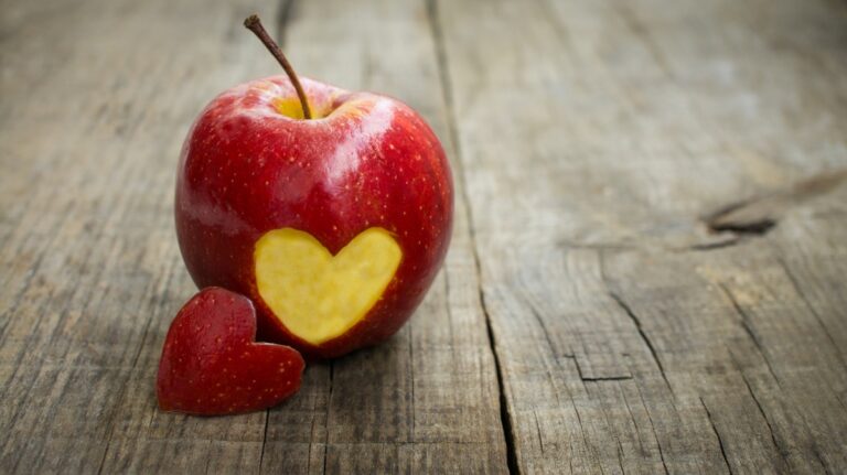 Red apple with one heart-shaped piece on wooden surface