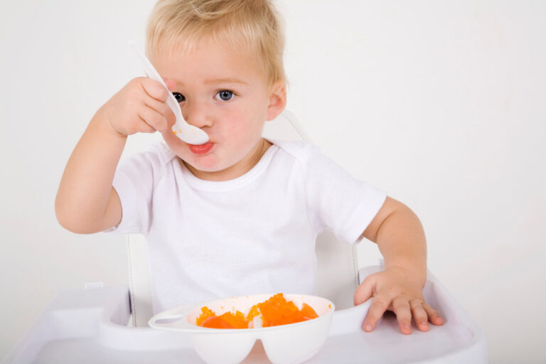 Baby eating muskmelon from the plate with a white plastic spoon