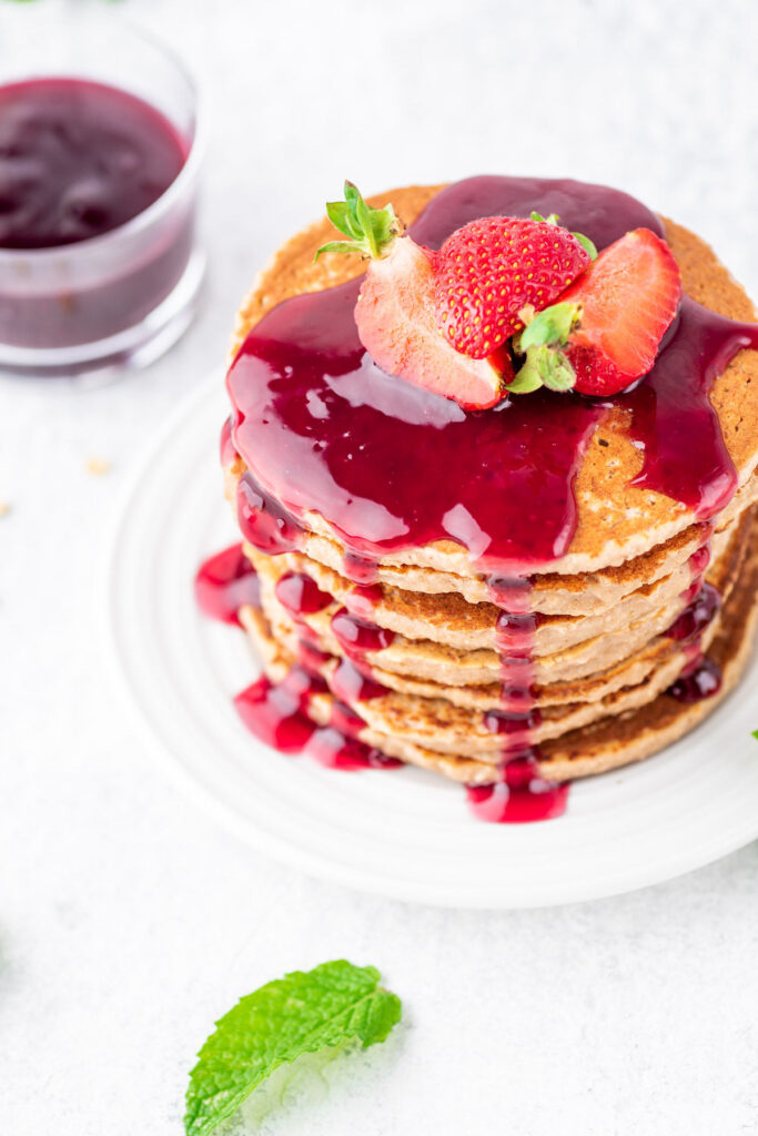 Peanut butter pancakes with jelly syrup stacked on each other, topped with sliced strawberries on a white plate