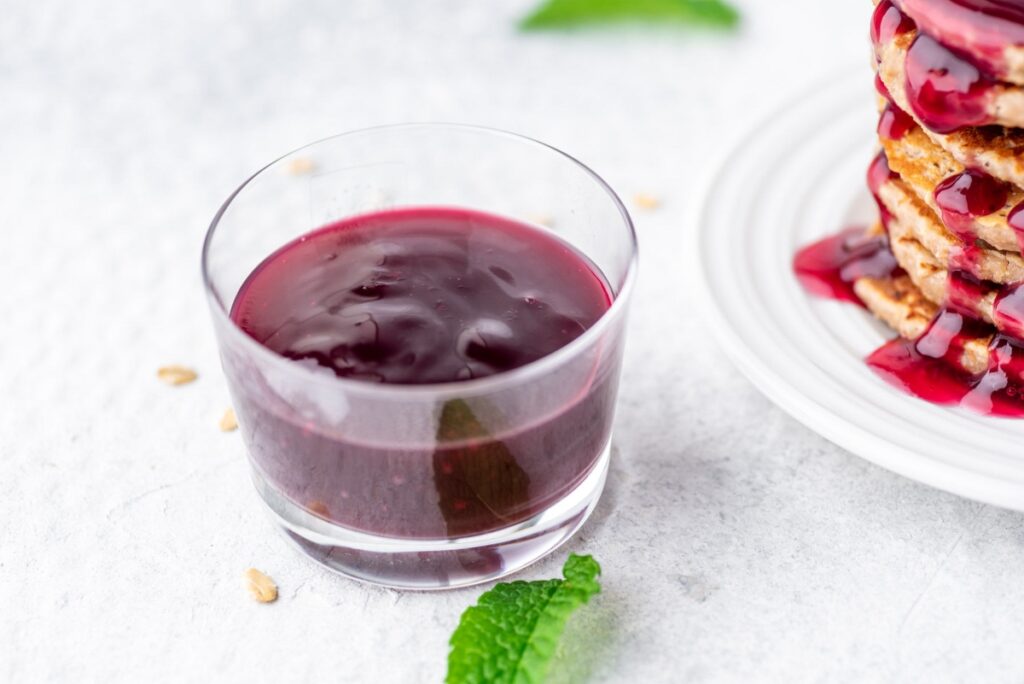 Jelly syrup in glass jar next to peanut butter pancakes stacked on each other on the white plate
