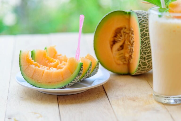 Muskmelon served on the plate with plastic fork, with juice in the glass beside the plate and muskmelon in the background