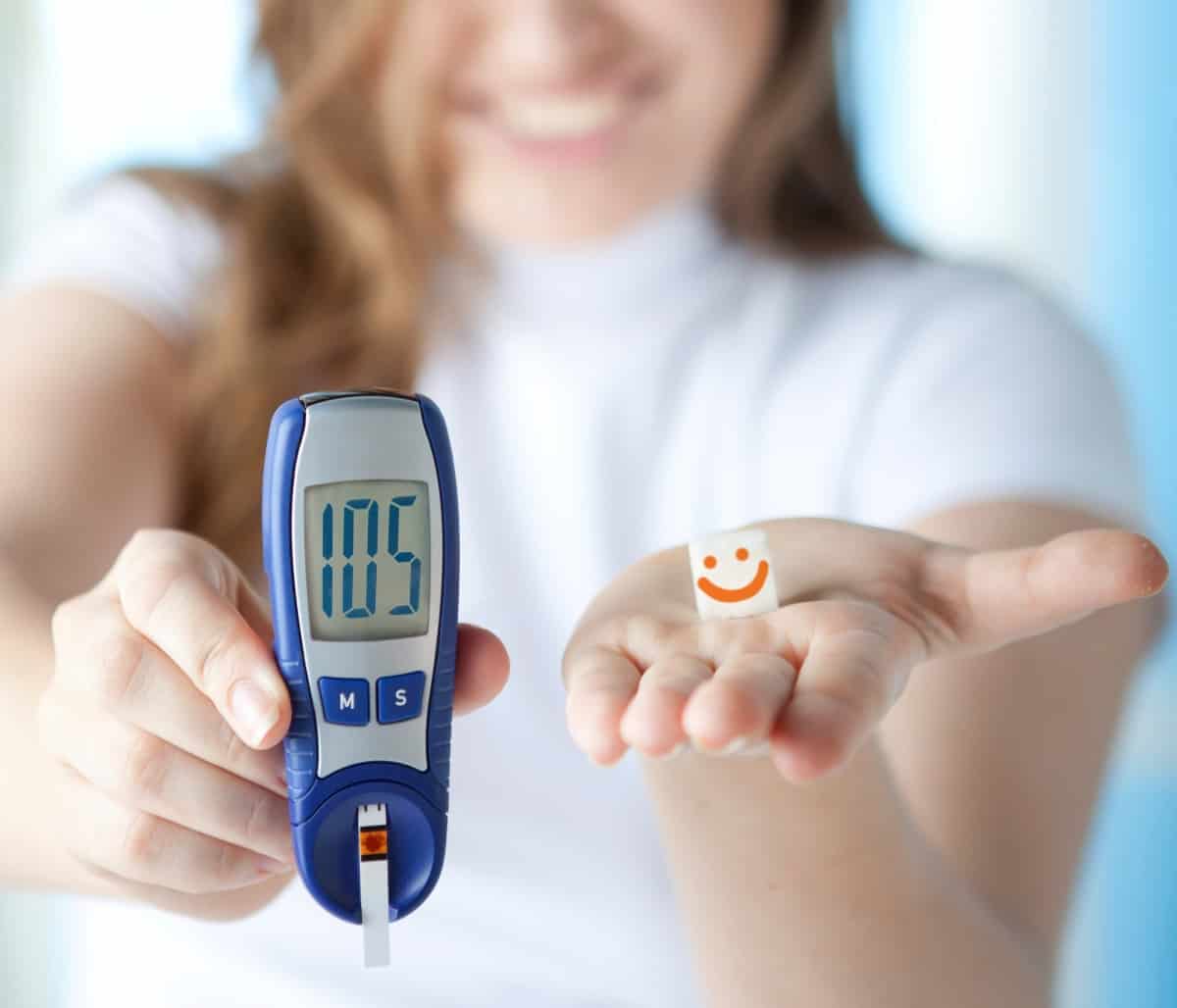 Woman holding glucometer in one hand and paper with smiley in other hand