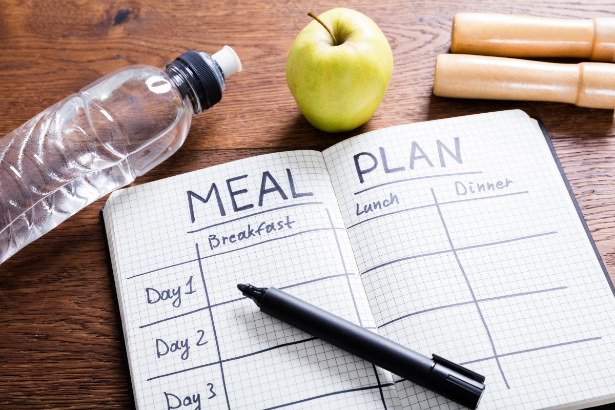 A meal plan notebook with a bottle of water, apple and, skip rope above it on the table