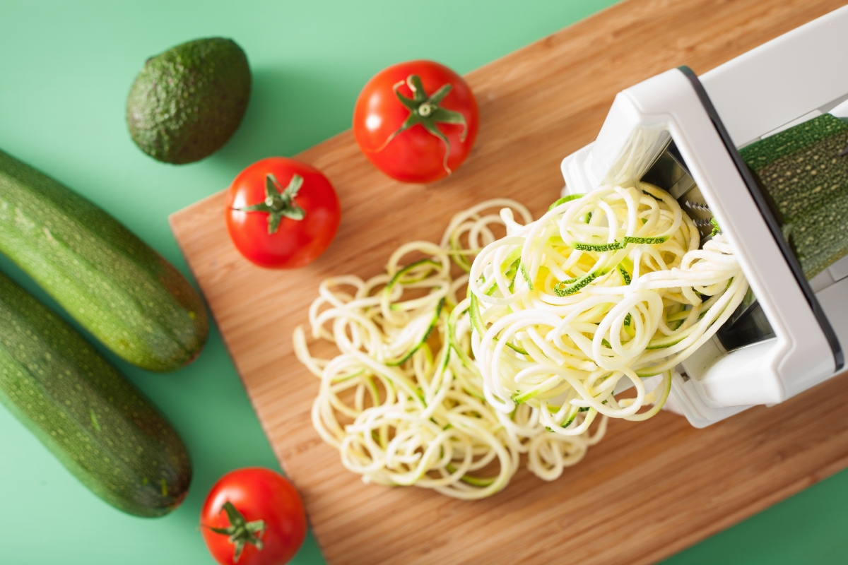 Spiralized veggie noodles on cutting board with tomatoes and zucchinis beside
