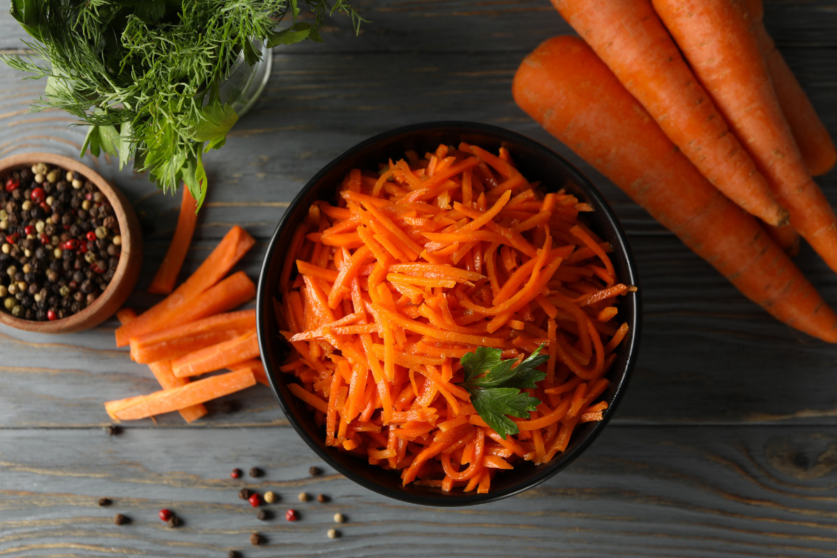 Carrot salad in a black bowl with chopped and whole carrots beside