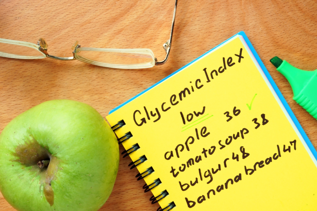 A notebook with Glycemic index calculations and a green apple and a pair of glasses beside