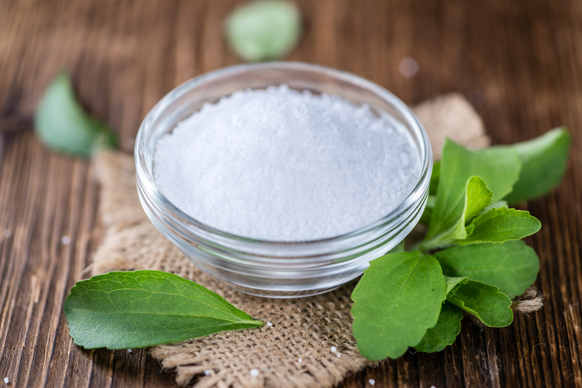Stevia granules in a cup on a cloth with stevia leaves spread around