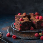 Healthy brownies with raspberries on a dark plate against the dark background