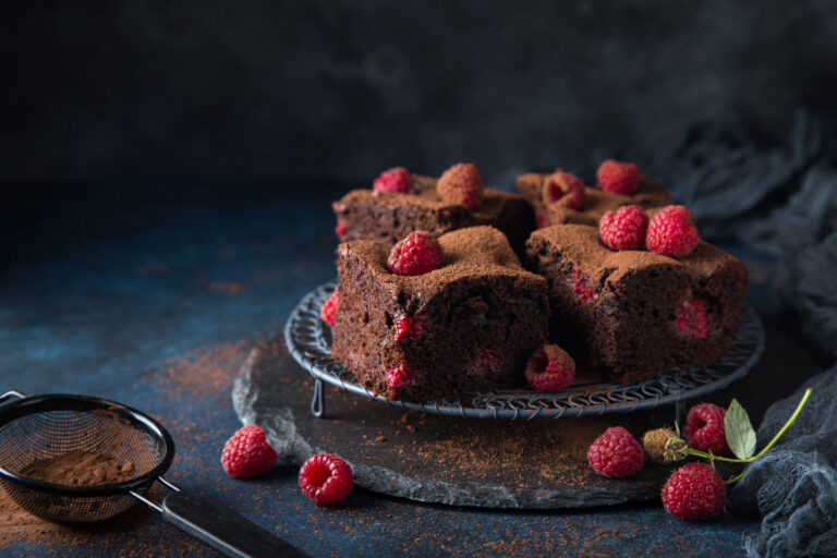 Healthy brownies with raspberries on a dark plate against the dark background